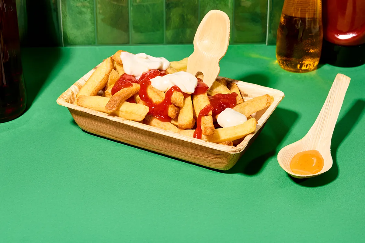 Anwendungsbeispiel Pommes Palmblatt-Container mit einer Portion Pommes mit May und Ketchup auf dunkelgrünem Hintergrund